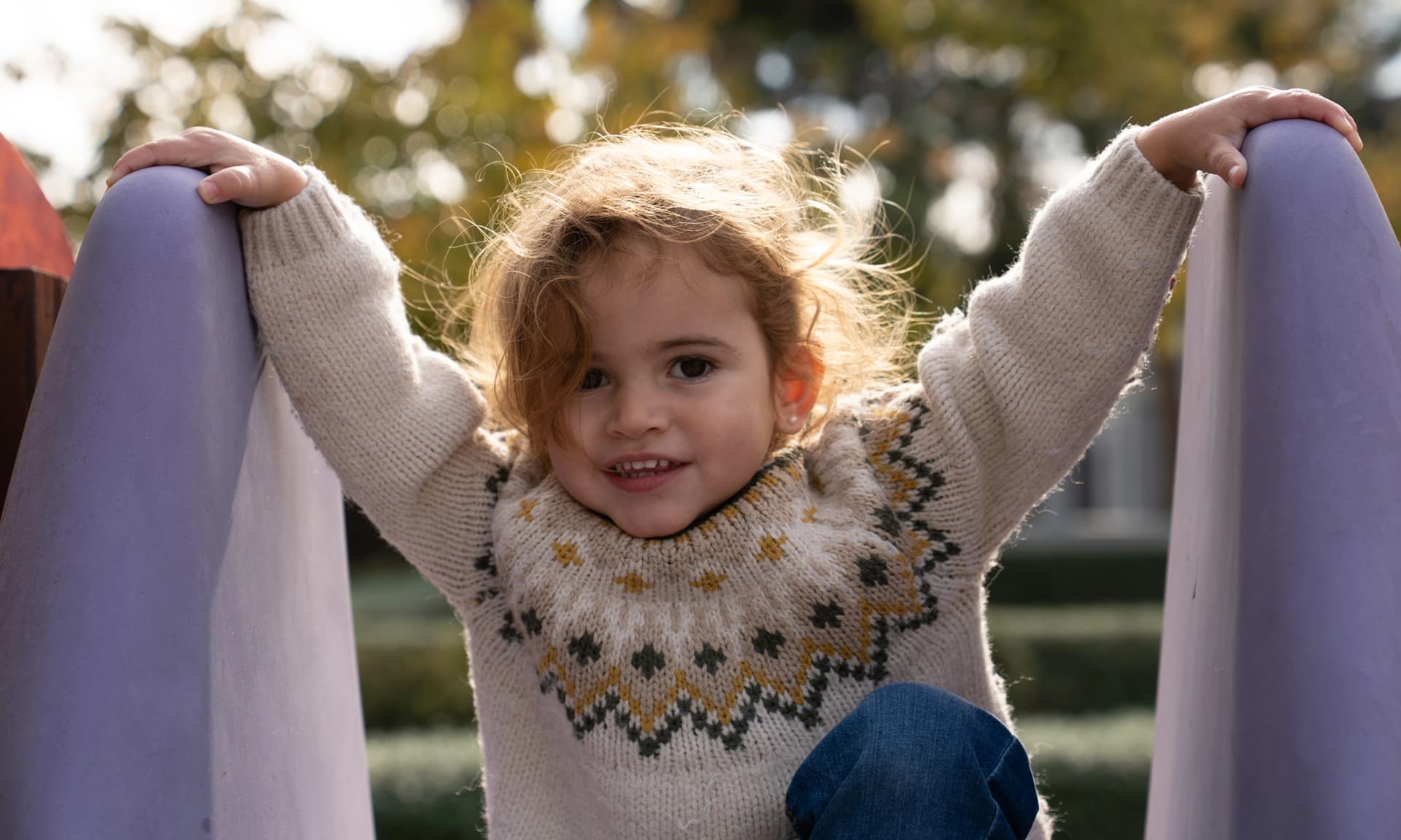 Imagen de una niña encima de un tobogán sonriendo a la cámara.